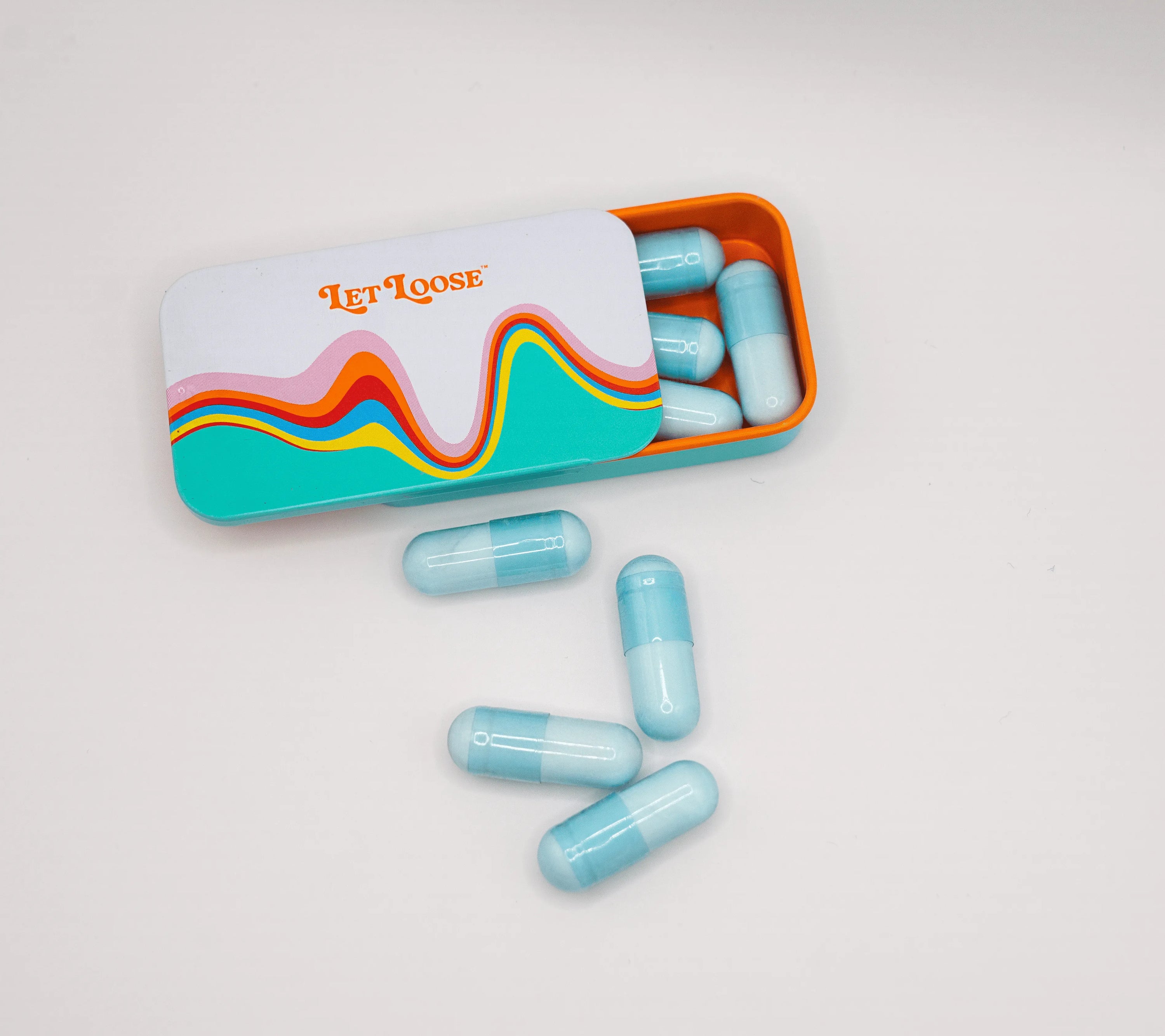 Open tin box labeled "Let Loose" with colorful design, containing light blue capsules, some scattered outside.